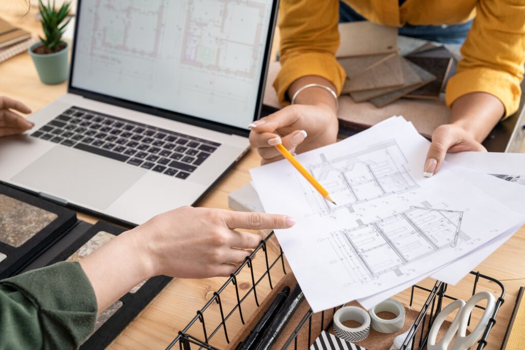 Hands of young female designer or architect pointing at paper with sketch of house while explaining some details to colleague at meeting