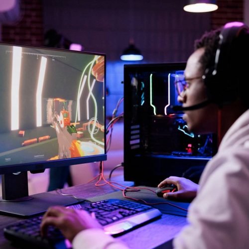 Young adult live streaming video games tournament on pc online with multiple players, playing action esport game on computer. Male streamer with headset enjoying gaming competition.